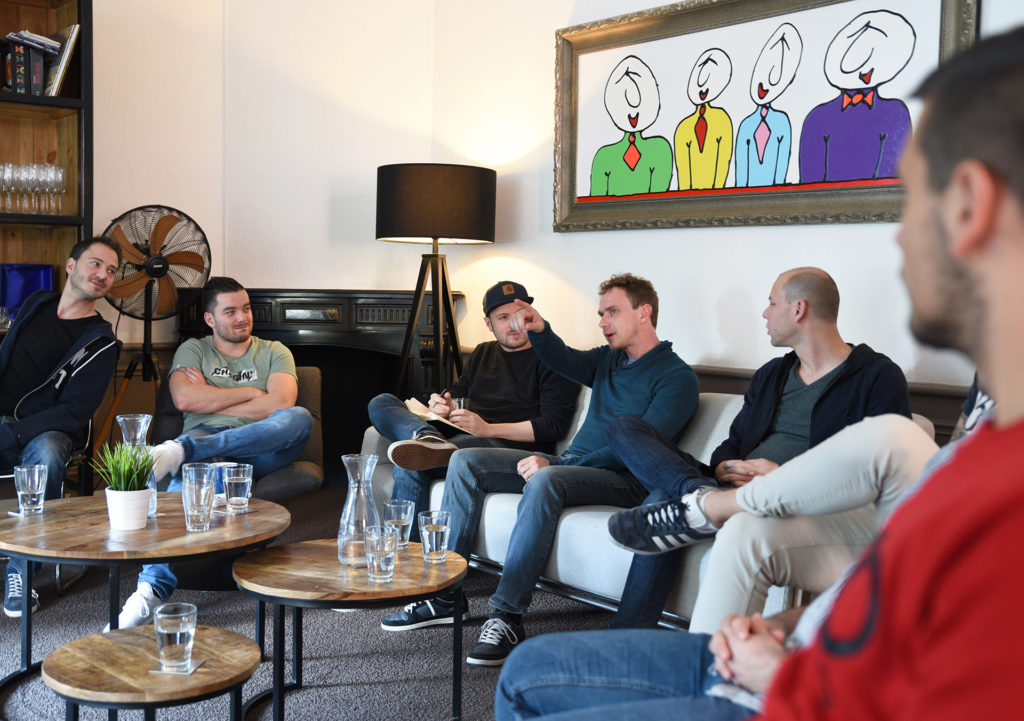 mensen op bank en stoelen, iemand wijst naar iets buiten de foto